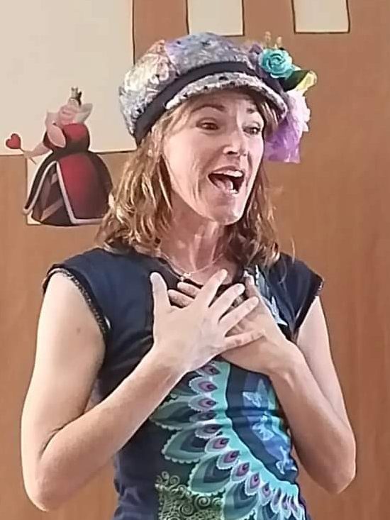 Araceli Lozano narrando un cuento, con las manos en el corazón y un sombrero de flores