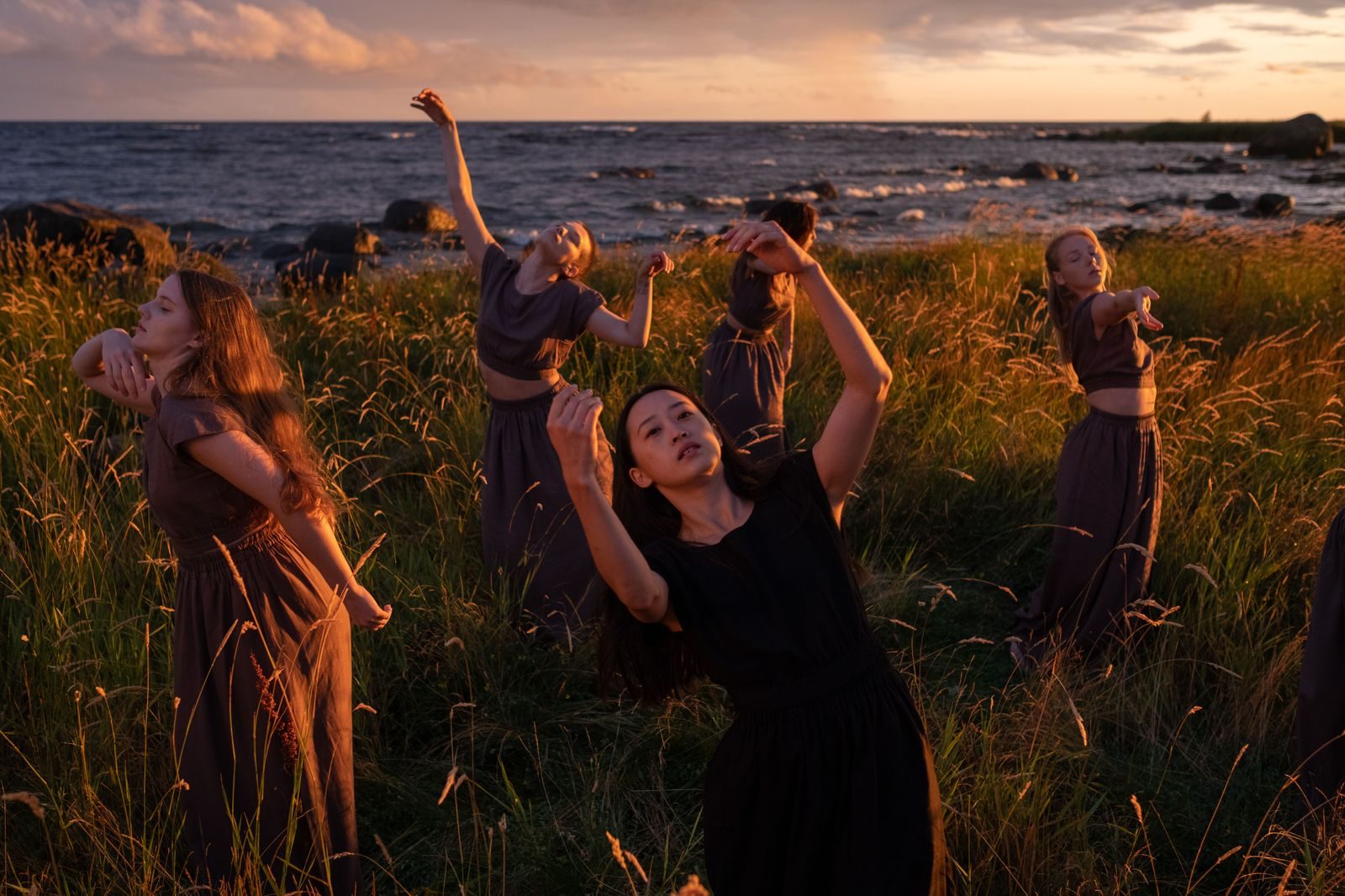 Mujeres en danza entre la hierba alta, junto al mar, al atardecer
