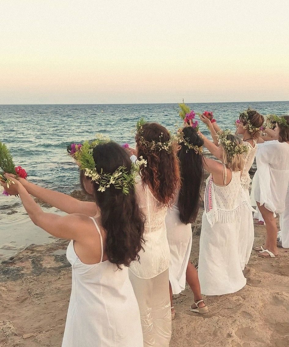 Mujeres de blanco con coronas de flores ofreciendo flores al mar al atardecer