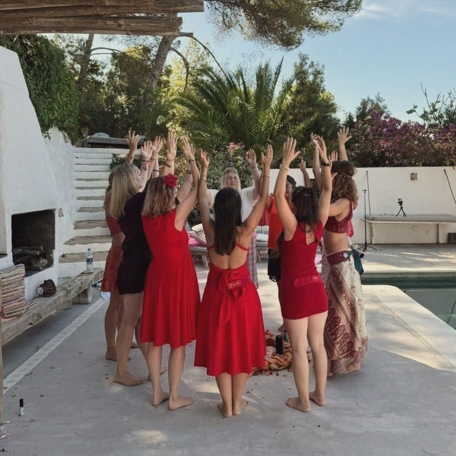 Círculo de mujeres vestidas de rojo con los brazos en alto