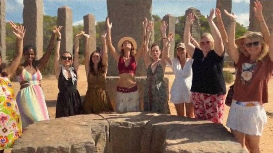 Grupo de mujeres con los brazos en alto entre columnas de piedra