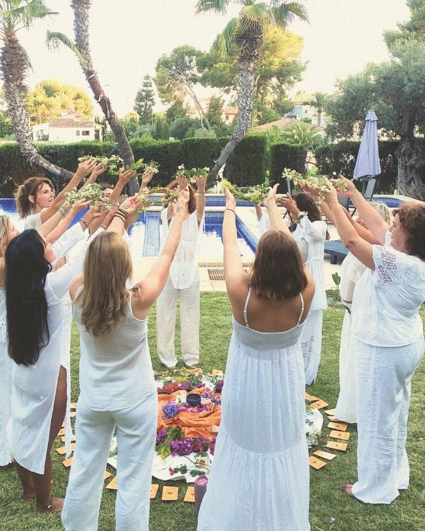 Mujeres vestidas de blanco en círculo, con los brazos en alto y coronas de flores